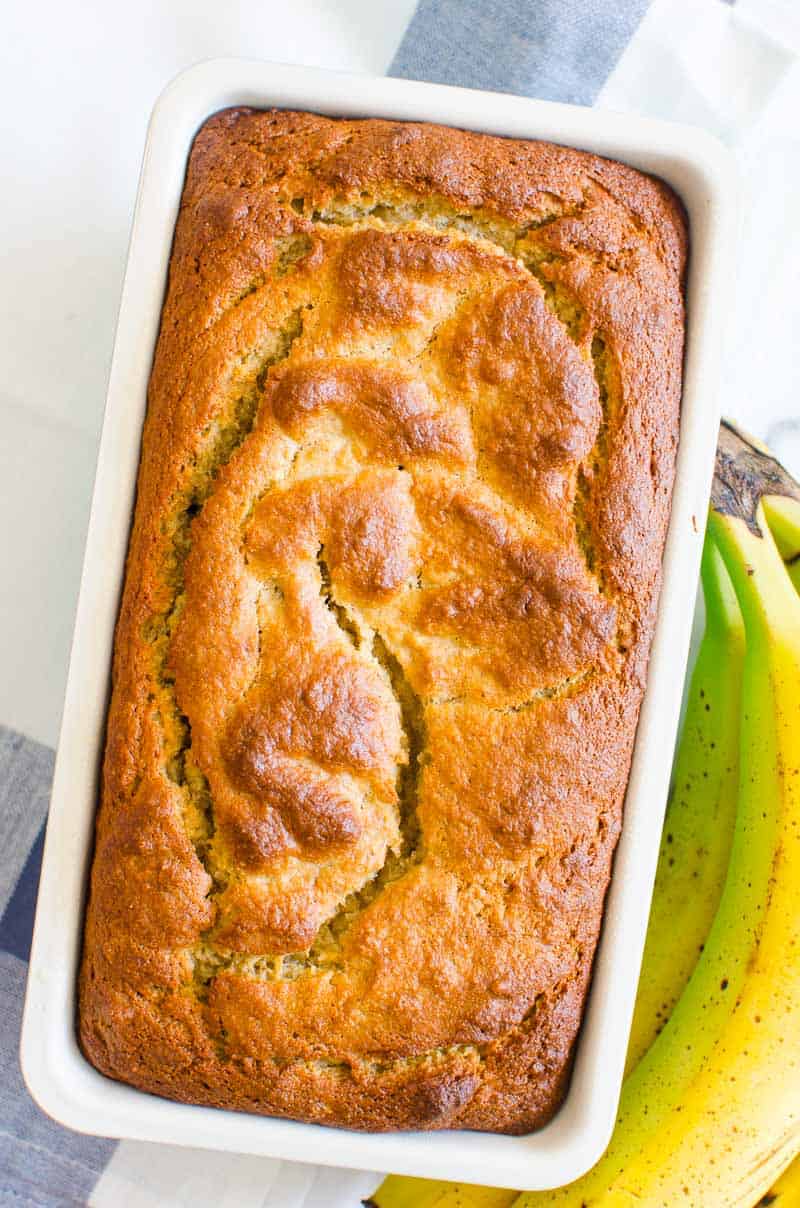 Almond flour banana bread in a loaf pan with bananas on a side.