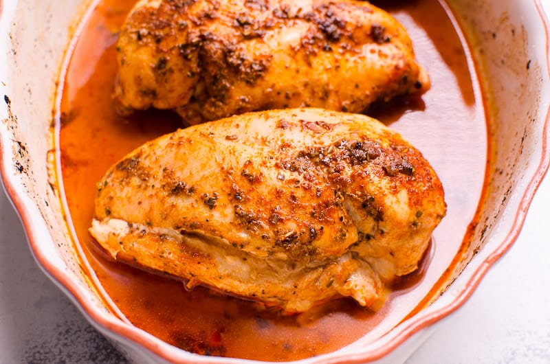 Oven baked chicken breasts in white baking dish with juices.
