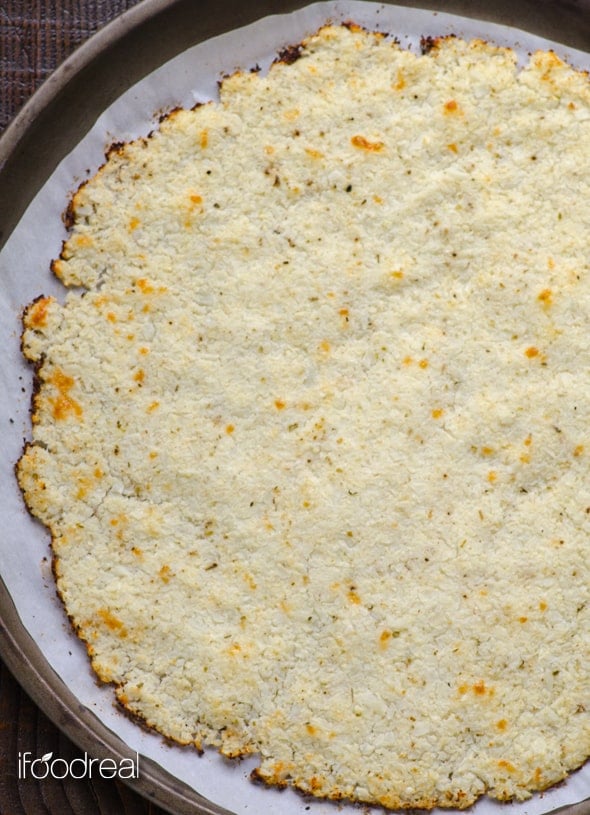 Baked cauliflower pizza crust on round baking sheet lined with parchment paper.
