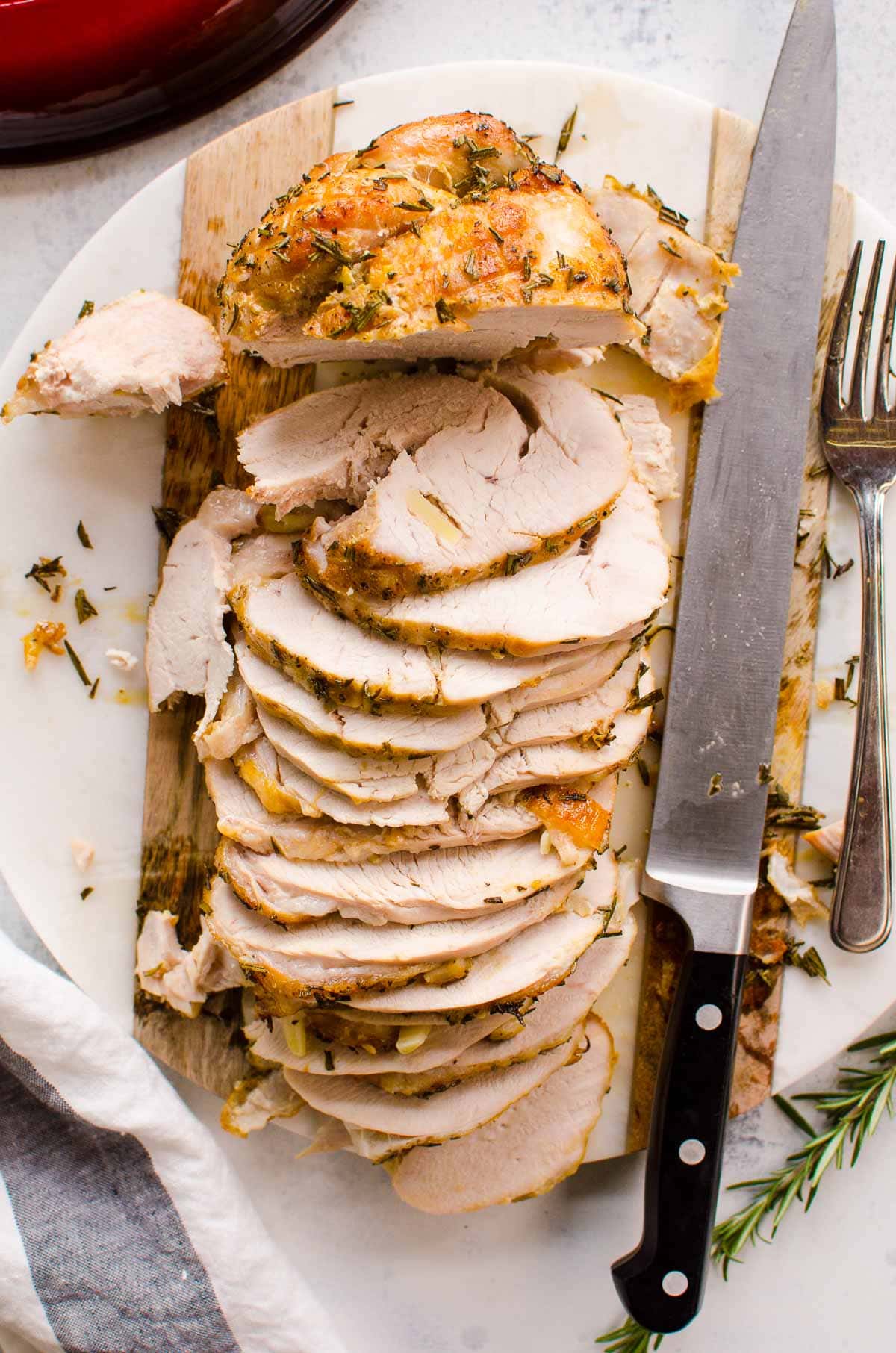 Boneless turkey breast roast sliced on a platter with knife and garnish.