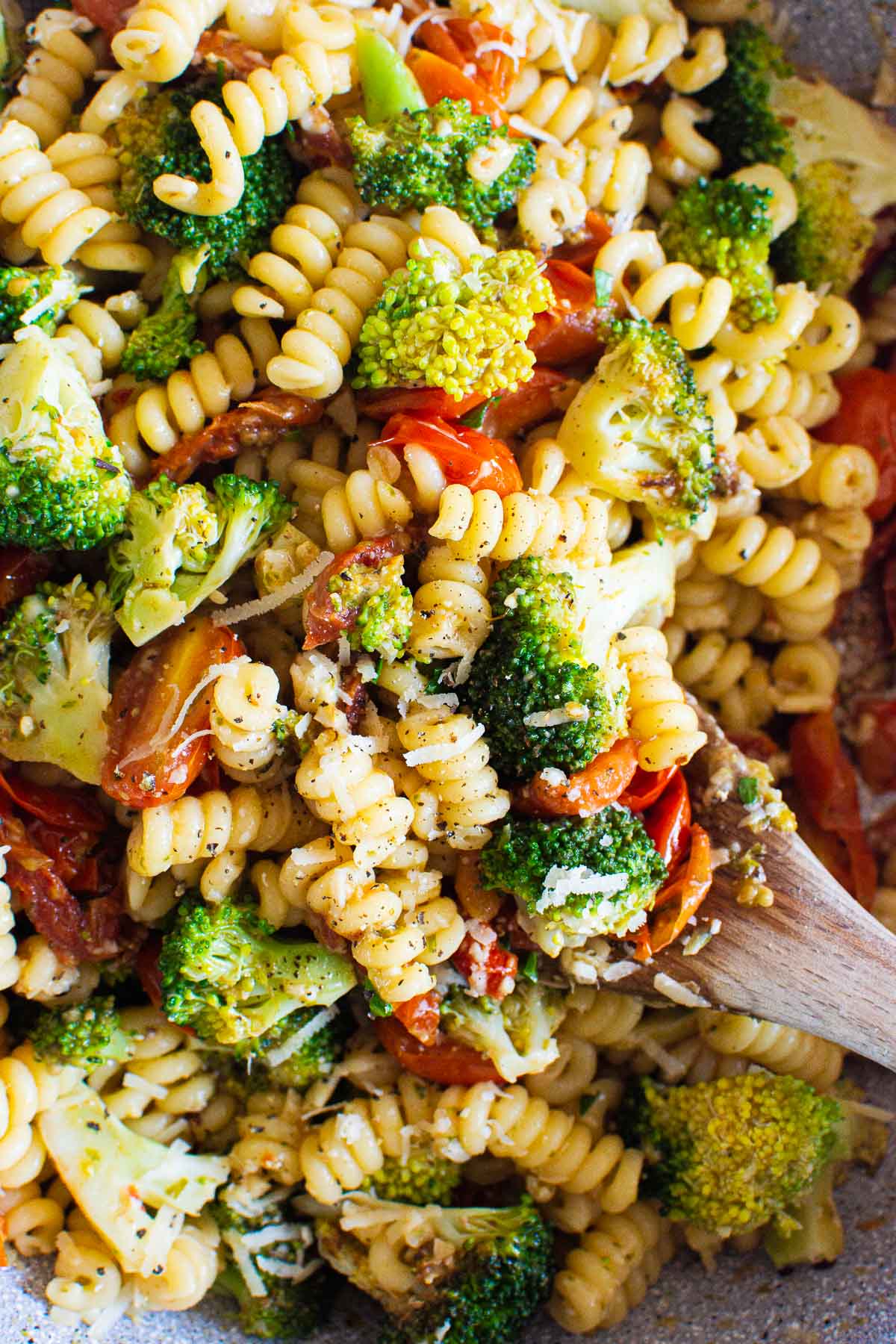 Close up of healthy pasta with broccoli and tomatoes on a wooden spoon.