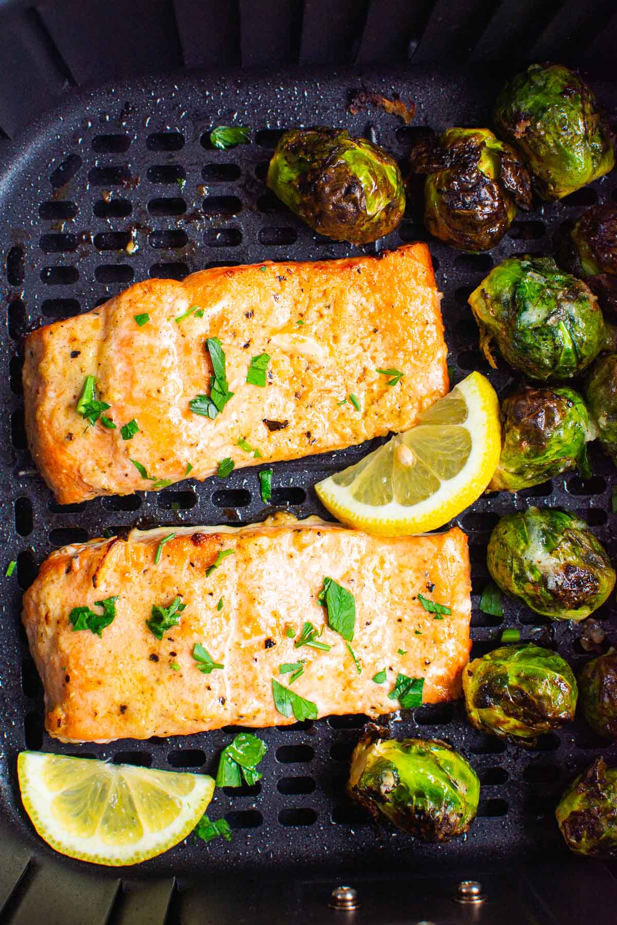 Two pieces of air fryer salmon with lemon and brussel sprouts.