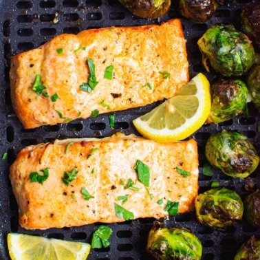 air fryer salmon in air fryer basked with brussels sprouts and lemon wedges