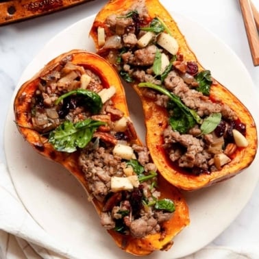 Two roasted butternut squash halves stuffed with apple sausage filling.
