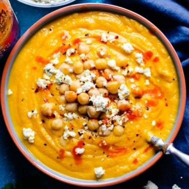 Buffalo cauliflower soup topped with chickpeas, blue cheese crumbles and hot sauce and served in a bowl with a spoon.