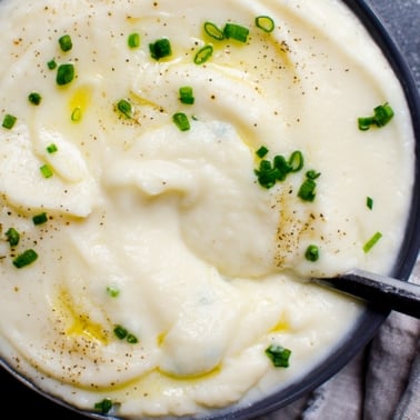 Cauliflower mashed potatoes with melted butter and chives in a bowl with a spoon.
