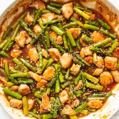 Chicken asparagus stir fry garnished with sesame seeds in a skillet.