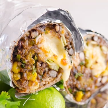 Chicken burritos wrapped in aluminum foil showing texture inside with melted cheese.