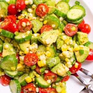 Avocado corn salad in a white bowl with serving utensils.