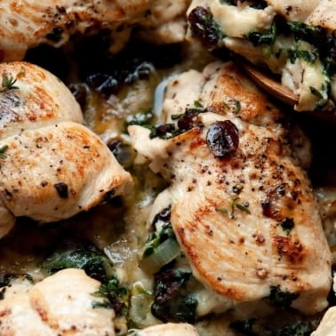 Chicken breasts stuffed with brie cheese, cranberries and spinach in sauce in a skillet.