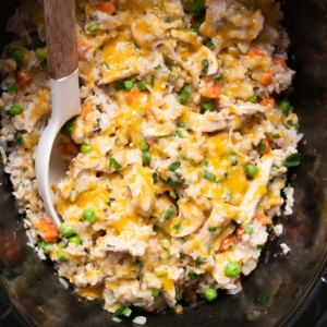 Crockpot chicken and rice with peas and carrots in black slow cooker with a spoon.