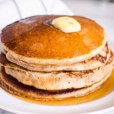 Whole wheat buttermilk pancakes with butter on top on white plate.