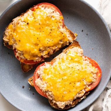 Two healthy tuna melt sandwiches with melted cheese and tomato on blue plate.