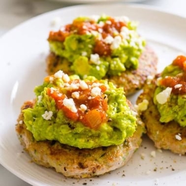Turkey burgers topped with guacamole and salsa on a plate.
