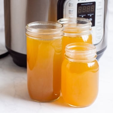 Instant Pot chicken broth in three glass jars with Instant Pot in the background.