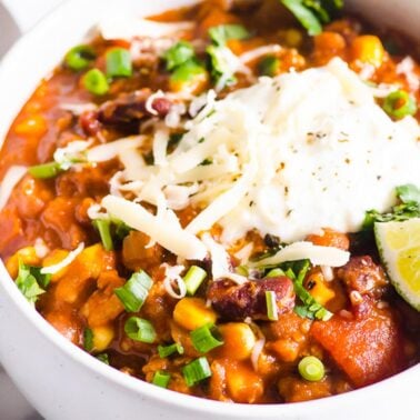 Instant Pot turkey chili garnished with sour cream, cheese and green onion in white bowl.