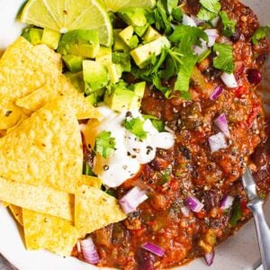 Instant Pot vegetarian chili in a bowl with tortilla chips, sliced lime, and cilantro.