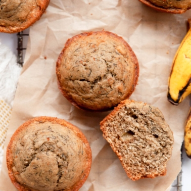 Two oat flour banana muffins and one sliced on parchment paper.