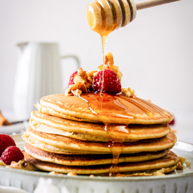 A stack of protein pancakes topped with berries and drizzled with honey.