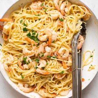 Shrimp spaghetti garnished with parsley and served in a skillet with tongs.