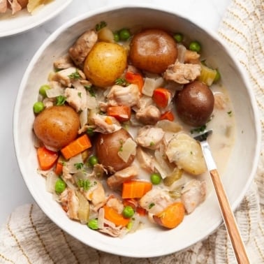 Slow cooker chicken stew with carrots and peas served in a bowl with a spoon.