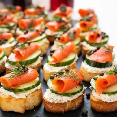Smoked salmon crostini with capers and dill on black platter.