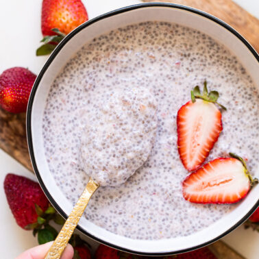 Strawberry chia pudding on a spoon above a bowl with more chia pudding garnished with fresh strawberries.