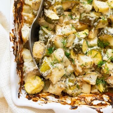Zucchini potato bake with melted cheese and fresh dill on top served in a baking dish with a spoon.