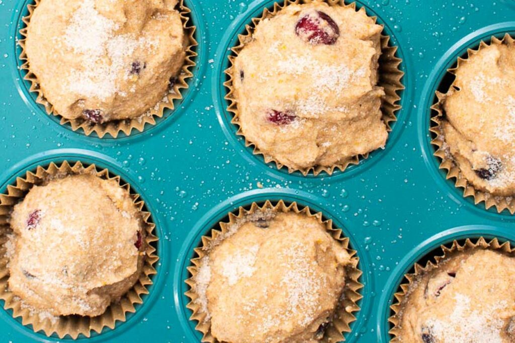 healthy cranberry orange muffins dusted with sugar and in blue muffin tin