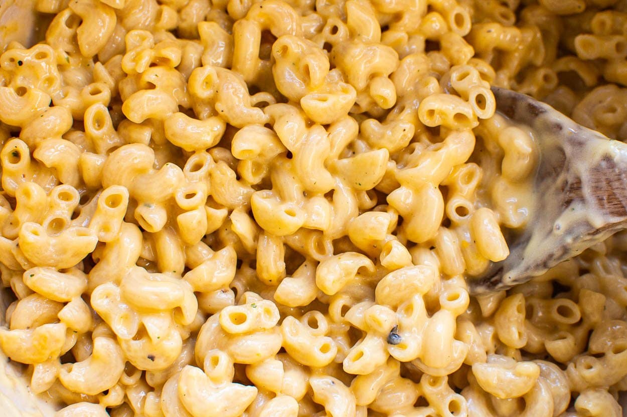 Healthy macaroni and cheese sprinkled with seasoning with a spoon dipped into it for serving.