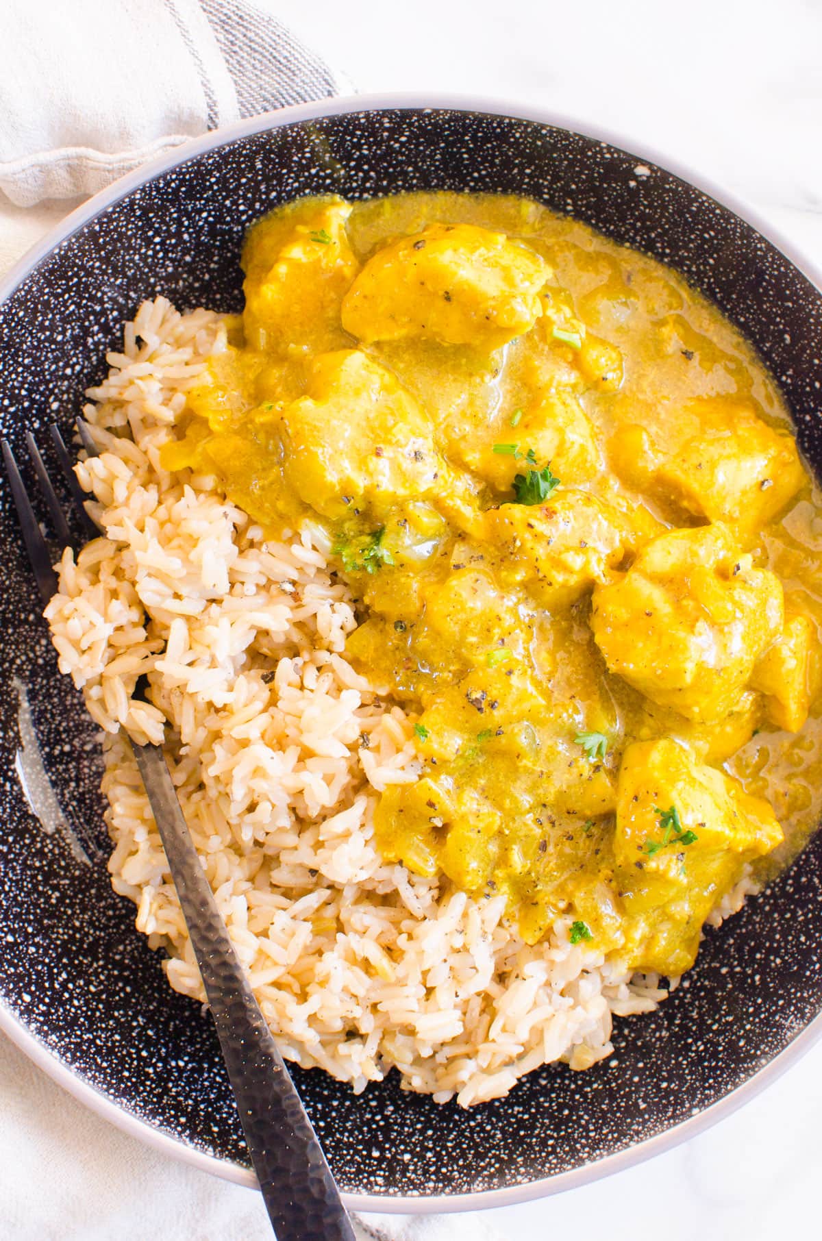 Chicken curry with brown rice in a black bowl.