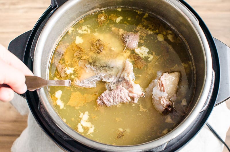 Broth and meat in Instant Pot with ladle.