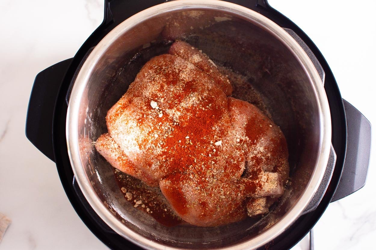 Whole chicken sprinkled with spices inside pressure cooker pot.