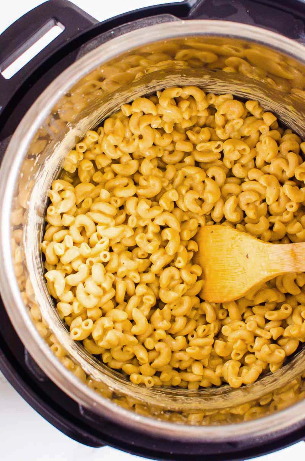 Mac and cheese in instant pot with a wooden spoon.