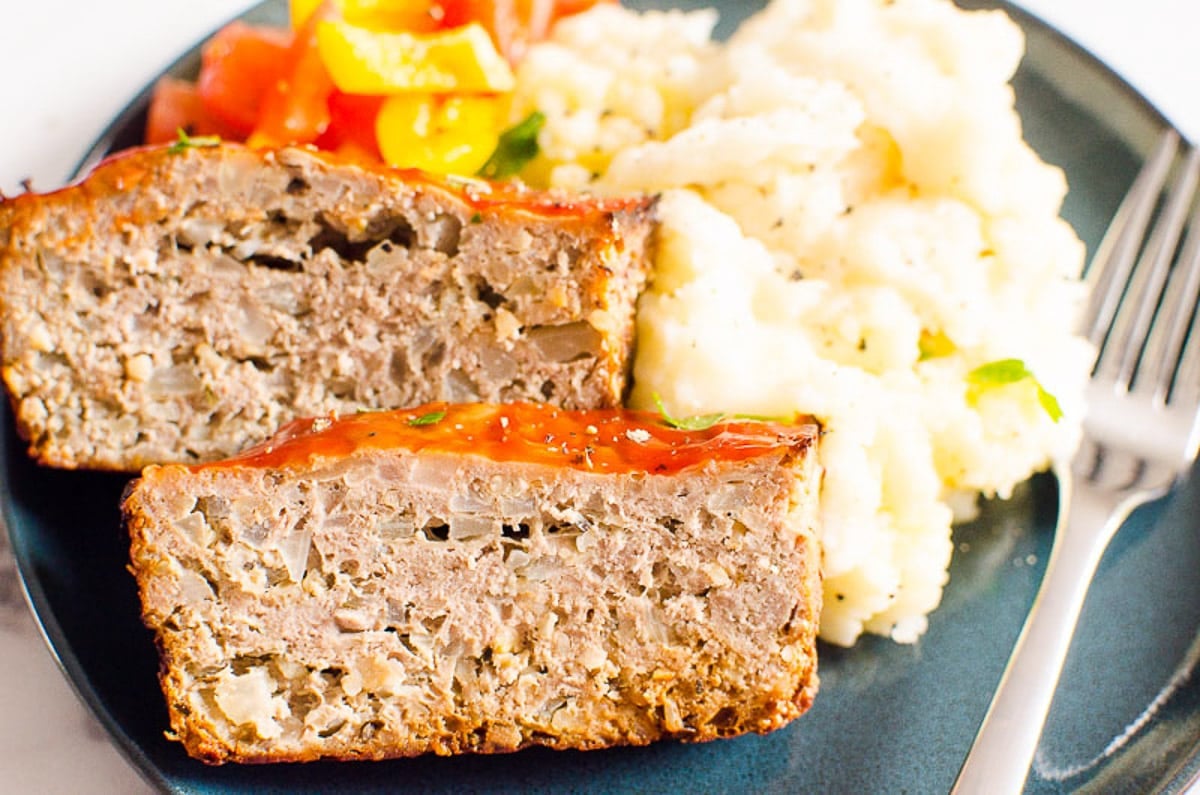 Mashed potatoes served with turkey meatloaf and bell pepper salad on a plate with a fork.