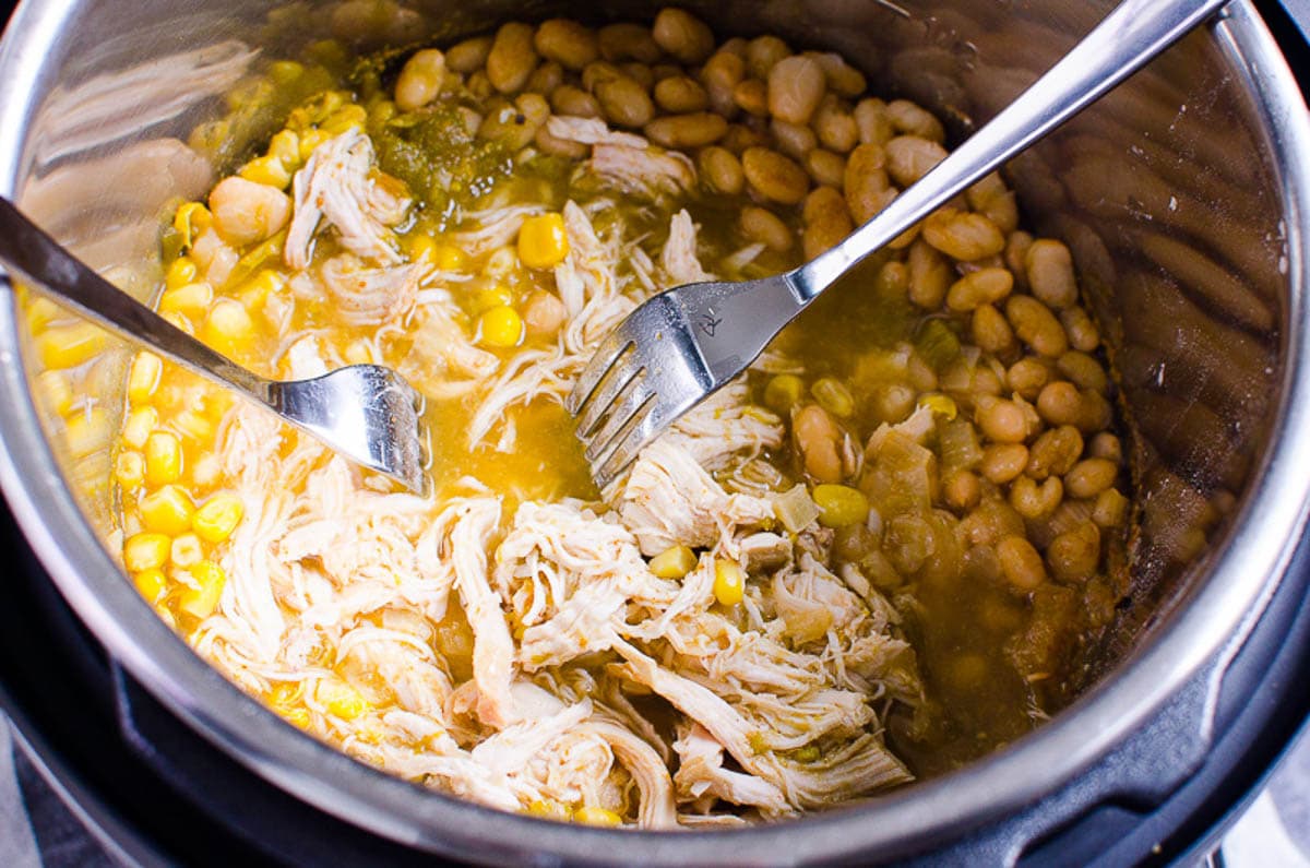 Shredding chicken with two forks in Instant Pot with corn and beans. 