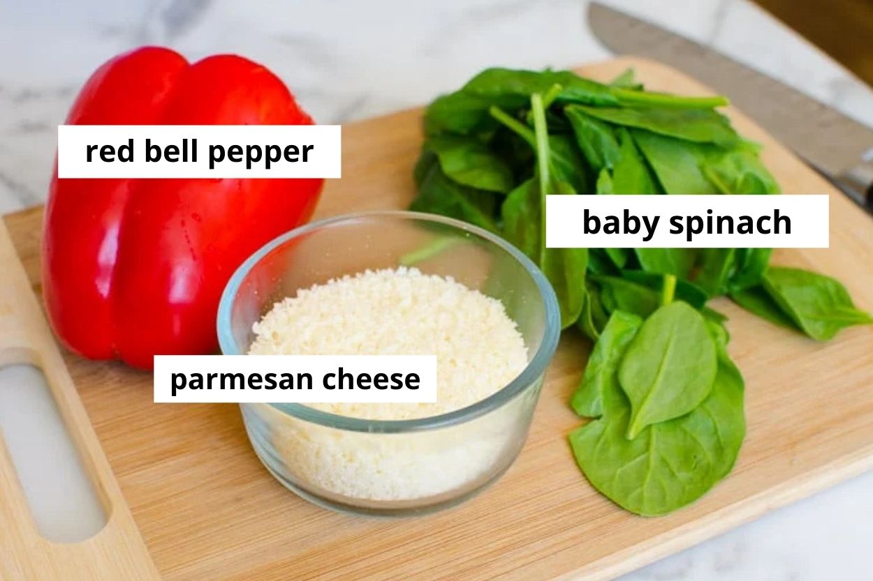 Red bell pepper, spinach and parmesan cheese on cutting board.