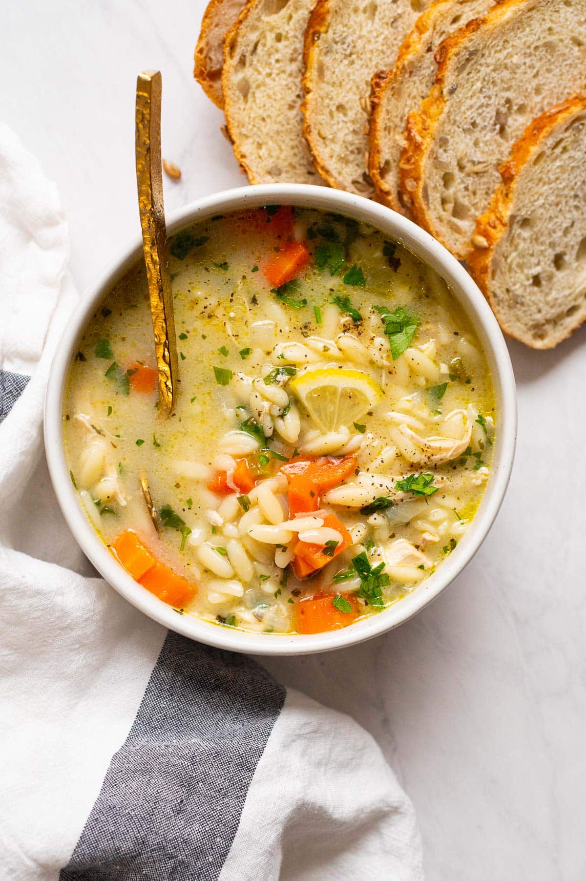Lemon chicken orzo soup served in a bowl with a golden spoon and bread slices.