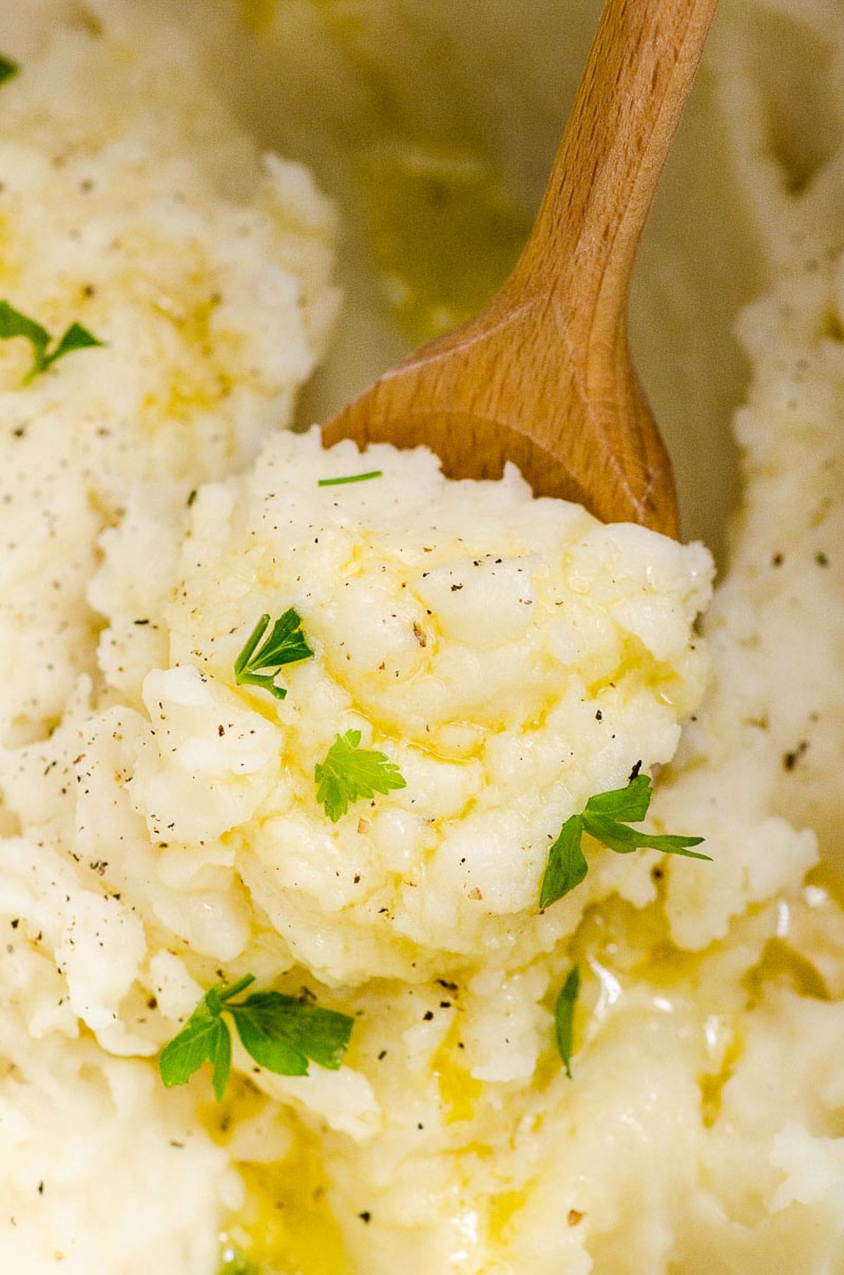 Close up of spoon inserted into mashed potatoes with butter and parsley.