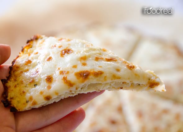 Hand holding a slice of cauliflower pizza crust with cheese.