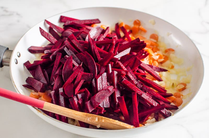 Sliced beets and chopped onion and carrots in a skillet.
